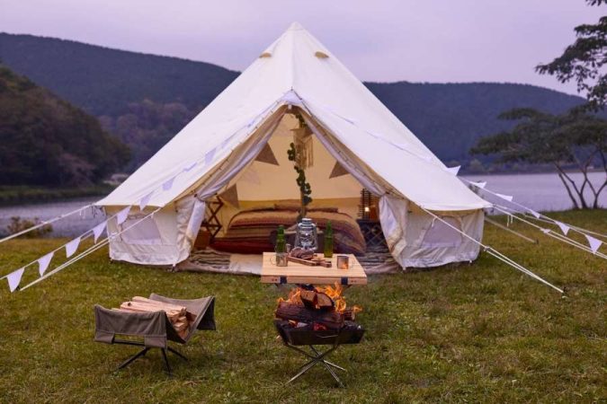 Une grande tente de glamping en toile blanche installée au bord d'un lac, bien différente d'une tente pliante publicitaire.