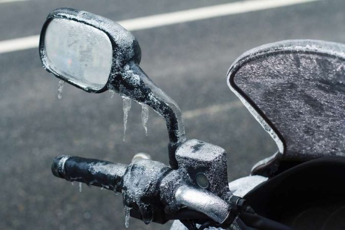Un rétroviseur et une nouvelle bulle de moto entièrement recouverts de glace en hiver.