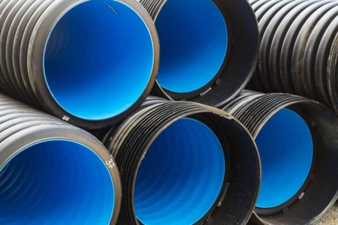 Empilement de grands tuyaux en plastique annelés de couleur noire à l'extérieur et bleue à l'intérieur, illustrant le choix du bon diamètre de tube en PVC pour l'assainissement.