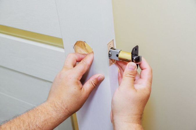 Les mains d'un bricoleur installant un nouveau cylindre de serrure sur une porte blanche.