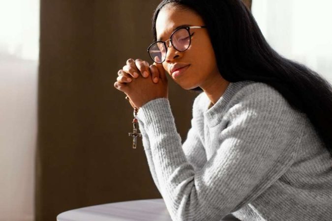 Une femme prie intensément en tenant un chapelet, un moment qui rappelle l'importance spirituelle d'une médaille de baptême pour adulte.